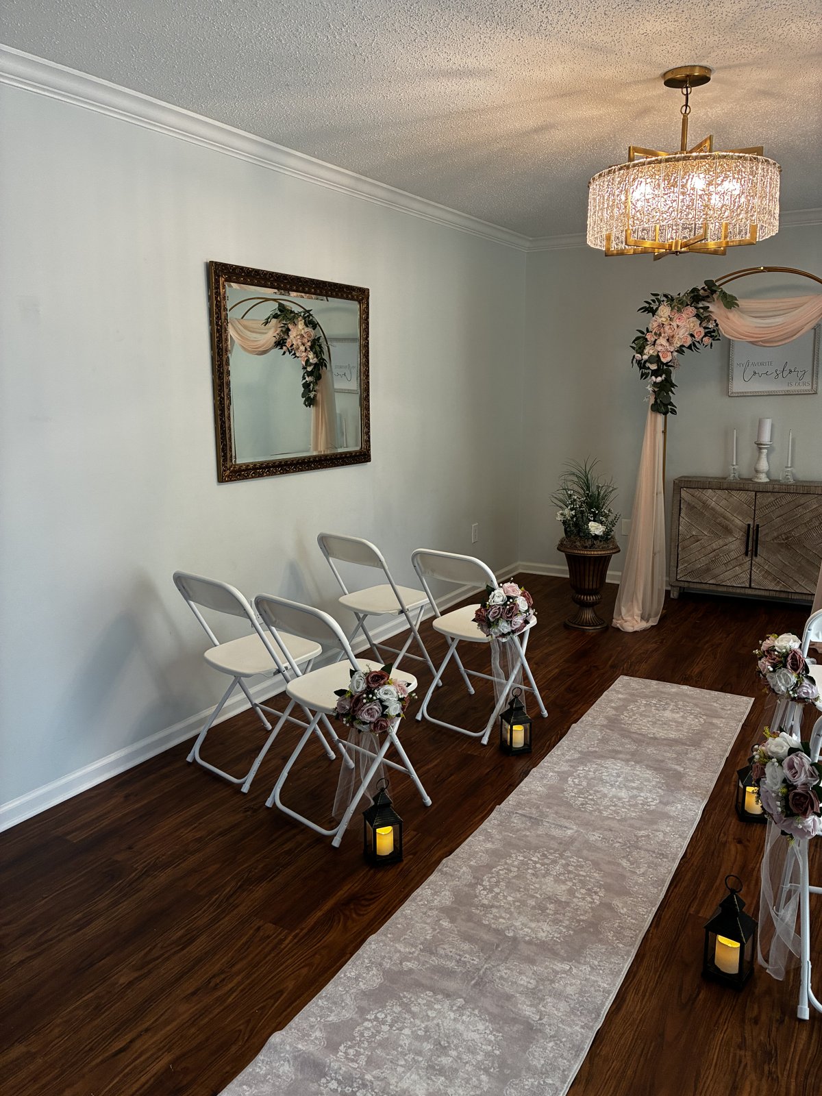 Side view of the ceremony room, with the blush draped arch, unity candles on a wooden cabinet, and a gold framed mirror on the wall